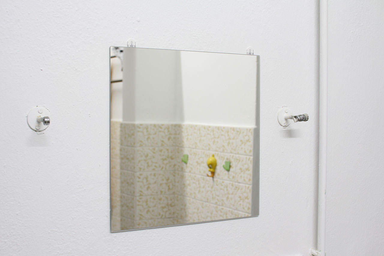 white wall with a piece of BLODLÖNN mirror, flanked by metal support arms for the old mirror